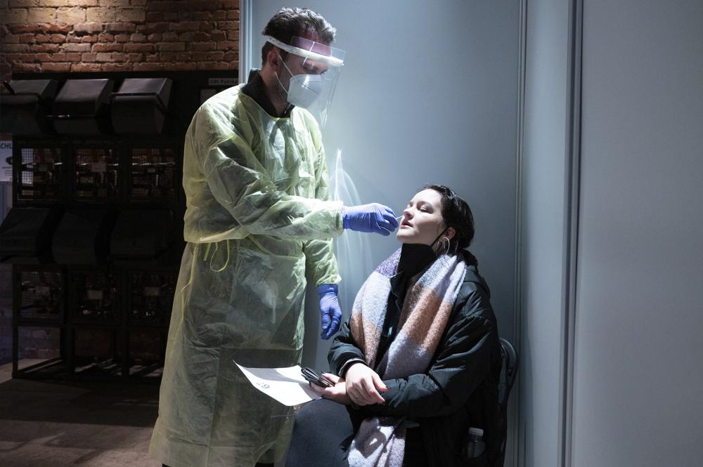 Max Walther, Test Center Manager, stands in front of Anna Overbeck during a Corona quick test at the Kulturarena Stromwerk in Dresden, Germany, Tuesday, Jan. 4, 2022. (Sebastian Kahnert/dpa via AP)