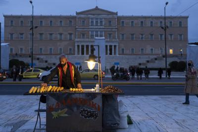 Un vendedor ambulante vende maíz frente al Parlamento griego en Atenas, el lunes 27 de diciembre de 2021. (AP Foto/Petros Giannakouris)