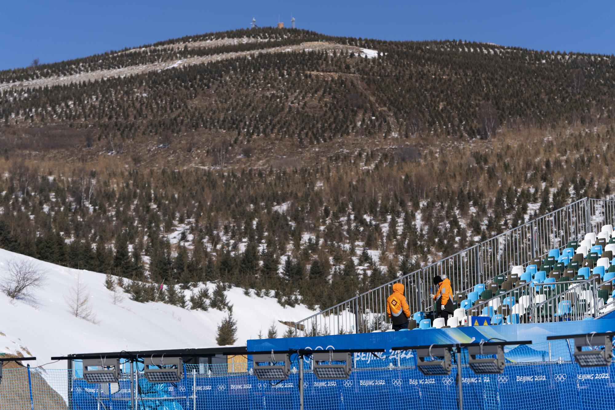 FILE - Two workers clean the stands near the halfpipe course ahead of the 2022 Winter Olympics, Jan. 27, 2022, in Zhangjiakou, China. Olympic athletes in Alpine skiing and other outdoor sports dependent on snow are worried as they see winters disappearing. (AP Photo/Jae C. Hong, File)