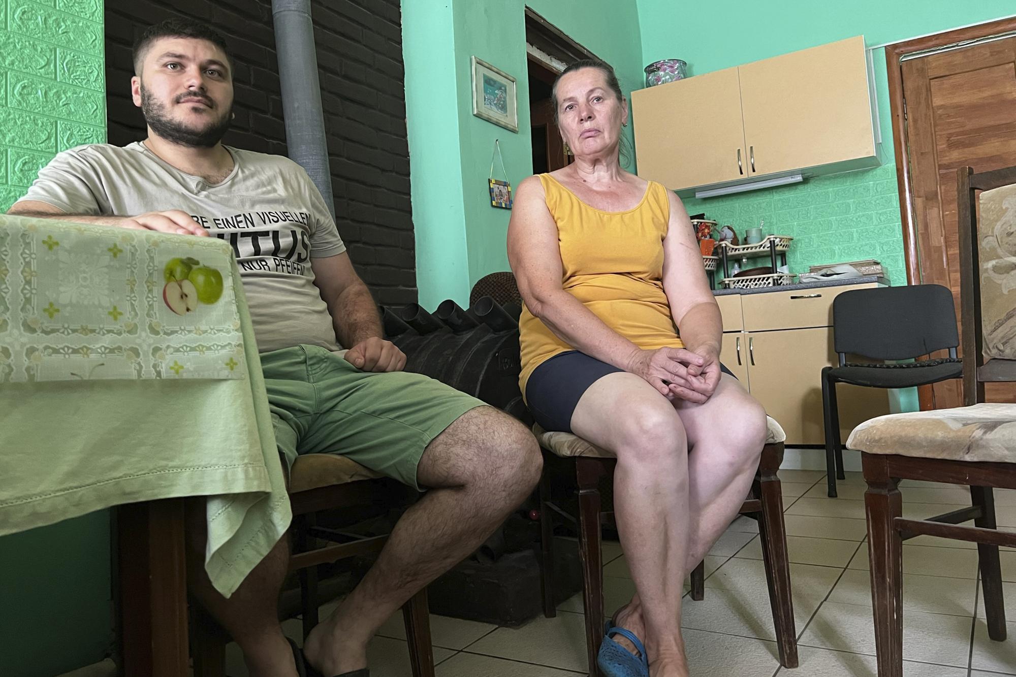 Andrii Shkoliar, left, and his mother-in-law, Natalia Savenko, sit in their home in Zdvyzhivka, Ukraine on Aug. 1, 2022. On March 18, Shkoliar and his wife were walking nearby to a relative's house when a dark-colored UAZ Patriot sped past, stopped abruptly and drove back to them. A soldier who appeared to be of higher rank stepped out of the Russian-made SUV, demanding to know why they'd broken curfew. "He told me: "I give you one hour back and forth, otherwise you'll be like this one in the car," Shkoliar recalled. (AP Photo/Erika Kinetz)