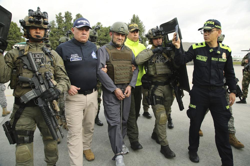 In this photo released by the Colombian Presidential Press Office, police escort Dairo Antonio Usuga, center, also known as Otoniel, leader of the violent Clan del Golfo cartel prior to his extradition to the U.S., at a military airport in Bogota, Colombia, Wednesday, May 4, 2022. (Colombian presidential press office via AP)