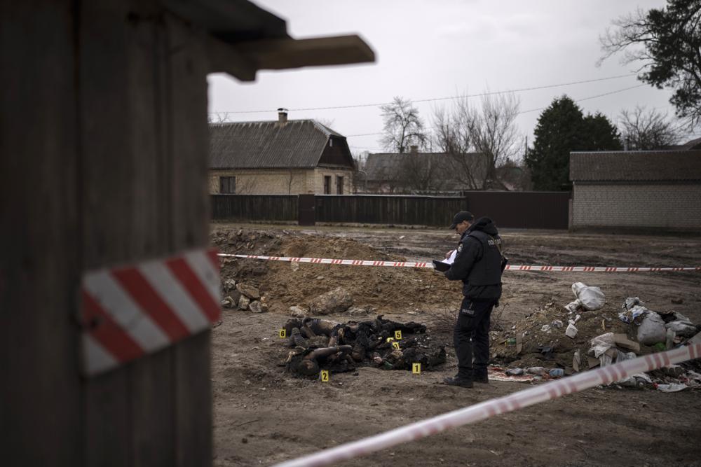 EDS NOTE: GRAPHIC CONTENT - A police officer stands next to six unidentified charred bodies lying on the ground at a residential area in Bucha, on the outskirts of Kyiv, Ukraine, Tuesday, April 5, 2022. Ukraine's president plans to address the U.N.'s most powerful body after even more grisly evidence emerged of civilian massacres in areas that Russian forces recently left. (AP Photo/Felipe Dana)