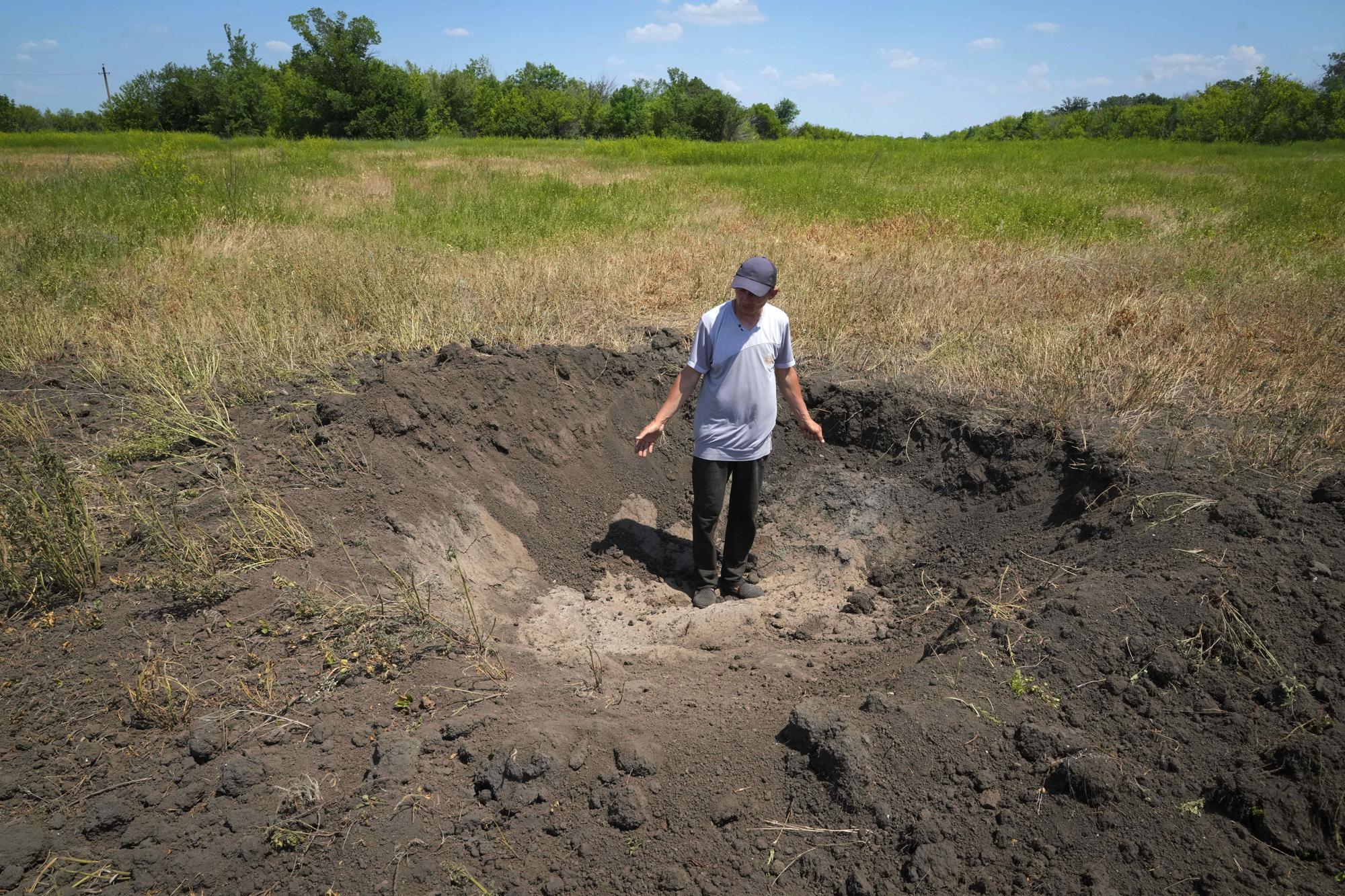 FILE - A farmer stands in a crater left by a Russian shell on his field in the village of Ptyche in eastern Donetsk region, Ukraine, Sunday, June 12, 2022. (AP Photo/Efrem Lukatsky, File)