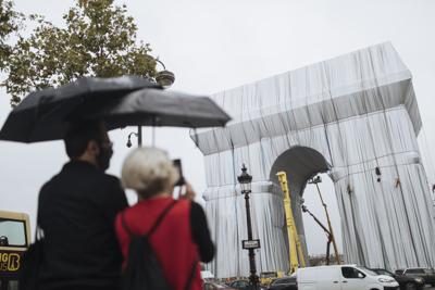 Dos personas miran cómo varios trabajadores envuelven en tela el monumento del Arco de Triunfo, el miércoles 15 de septiembre de 2021. (AP Foto/Lewis Joly)