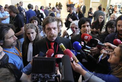 El cantante de Eagles of Death Metal, Jesse Hughes, en el centro, y el guitarrista Eden Galindo, en el centro a la derecha, responden preguntas de la prensa afuera de un tribunal en París el martes 17 de mayo de 2022. Los músicos comparecieron en la corte para testificar sobre la noche en que extremistas del Estado Islámico irrumpieron en su concierto en el teatro Bataclan y mataron a decenas de personas en el peor ataque terrorista en Francia en generaciones. (Foto AP/Christophe Ena)