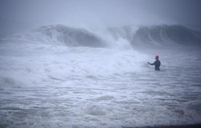 Matt Prue, de Stonington, Connecticut, camina en el Océano Atlántico para surfear las olas de la tormenta tropical Henri mientras el sistema se aproximaba, en Rhode Island, el domingo 22 de agosto de 2021. (AP Foto/Stew Milne)