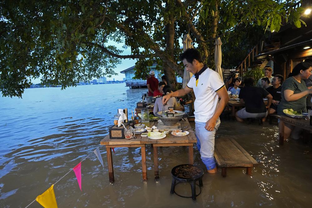 Customers of the riverside Chaopraya Antique Café enjoy themselves despite the extraordinary high water levels in the Chao Phraya River in Nonthaburi, near Bangkok, Thailand, Thursday, Oct. 7, 2021. The flood-hit restaurant has become an unlikely dining hotspot after fun-loving foodies began flocking to its water-logged deck to eat amid the lapping tide. Now, instead of empty chairs and vacant tables the “Chaopraya Antique Café” is as full as ever, offering an experience the canny owner has re-branded as “hot-pot surfing.” (AP Photo/Sakchai Lalit)