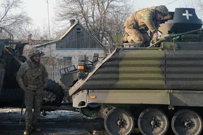 Un soldado ucraniano se ve de pie junto a un vehículo militar en el que trabaja otro soldado, en una calle en la ciudad de Kramatorsk, en la región de Donestk, Ucrania, el domingo 19 de febrero de 2023. (AP Foto/Alex Babenko)