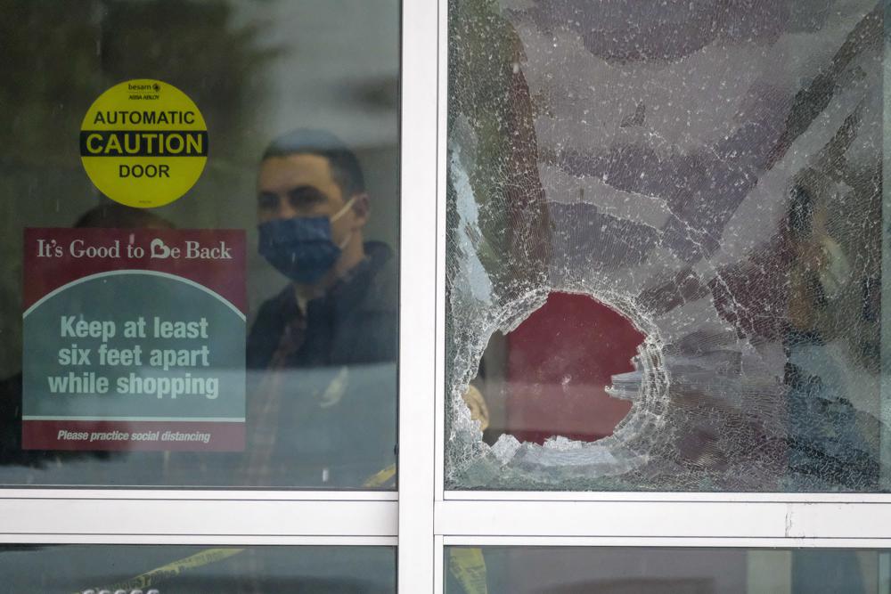 Seorang petugas polisi bekerja di balik pintu kaca yang pecah di tempat kejadian di mana dua orang terkena tembakan dalam penembakan di toko Burlington Coat Factory di Hollywood Utara, California, Kamis, 23 Desember 2021. (AP Photo/Ringo HW Chiu )