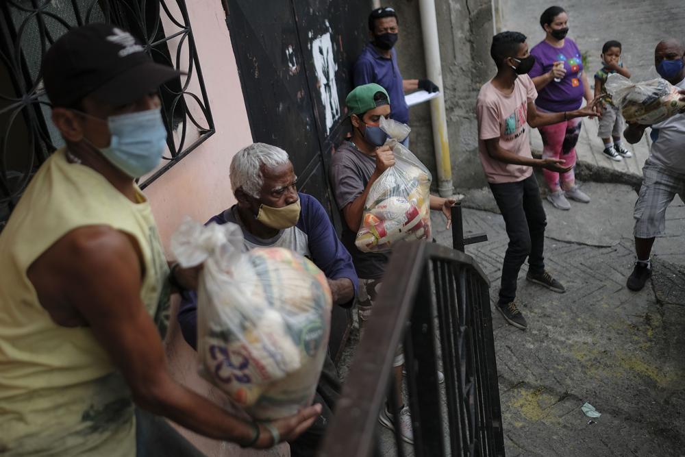 FILE - In this April 10, 2021 file photo, residents help unload bags of basic food staples, such as pasta, sugar, flour and kitchen oil, provided by a government food assistance program called CLAP, or Local Committees of Supply and Production, in the Santa Rosalia neighborhood of Caracas, Venezuela. Despite repeated multiplications of the official minimum wage earned by millions of Venezuelans, it still amounts to about $2, not enough to buy a kilogram of chicken. (AP Photo/Matias Delacroix, File)