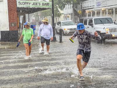 Peatones pasan por el cruce entre las calles Greene y Duval en medio de fuertes vientos y lluvias asociadas a la tormenta tropical Elsa a su paso por Cayo Hueso, Florida, el martes 6 de julio de 2021. (Rob O'Neal/The Key West Citizen via AP)