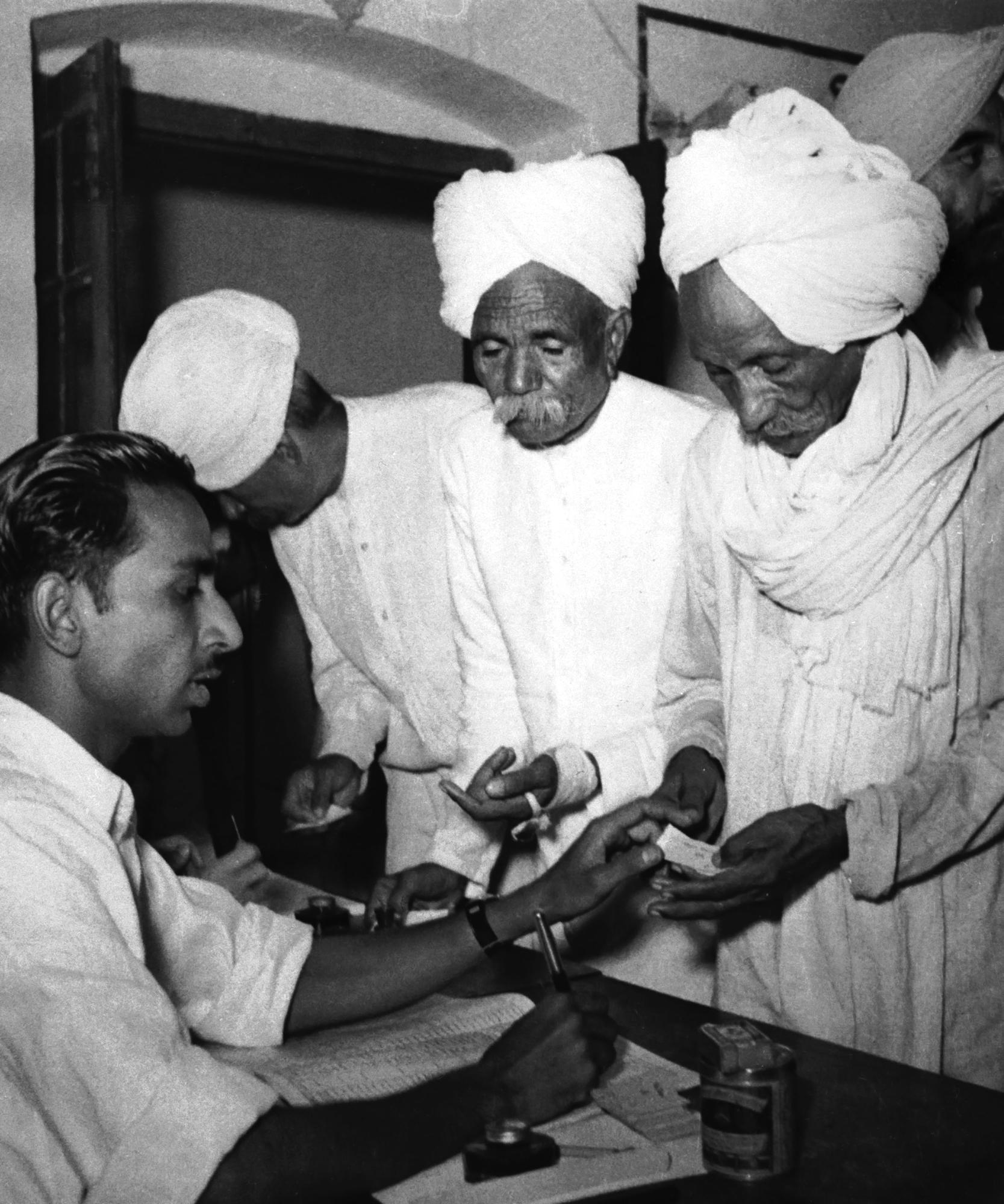 ARQUIVO - Eleitores recebem cédulas de funcionários das assembleias de voto para a primeira eleição geral da Índia em uma vila rural do estado de Delhi na Índia por volta de 14 de dezembro de 1951. (AP Photo/File)