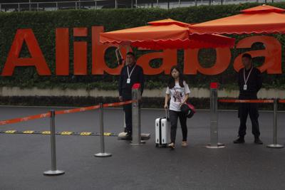 Una mujer lleva una maleta mientras pasa entre guardias de seguridad en la entrada de la sede de la compañía Alibaba en Hangzhou, en China, el 27 de mayo de 2016. (AP Foto/Ng Han Guan)
