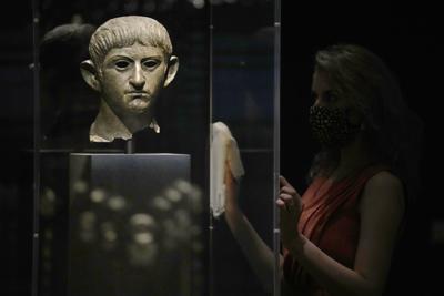 Una empleada del Museo Británico posa junto a una cabeza de bronce del emperador romano Nerón que data del año 54-61  y que fue hallada en el río Alde en Rendham en Suffolk, en el este de Inglaterra, durante una presentación a la prensa de la exposición "Nerón: el hombre detrás del mito" el lunes 24 de mayo de 2021 en Londres. (AP Foto/Matt Dunham)