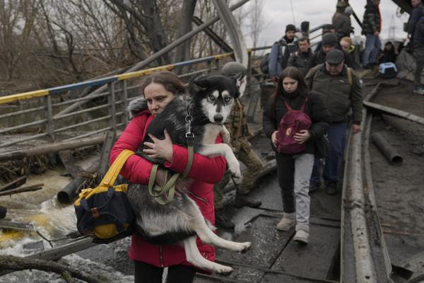 Una mujer sostiene a un perro mientras cruza el río Irpin en un camino improvisado debajo de un puente mientras la gente huye de la ciudad de Irpin, Ucrania, el sábado 5 de marzo de 2022. (AP Foto/Vadim Ghirda)