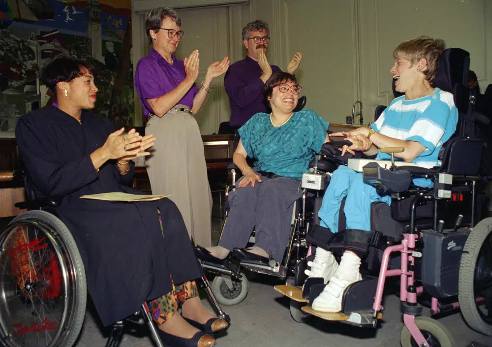 FILE - Judy Heumann, center, is applauded during her swearing-in as U.S. Assistant Secretary for Special Education and Rehabilitative Service by Judge Gail Bereola, left, in Berkeley, Calif., on Tuesday, June 29, 1993. Standing at left is Berkeley Mayor Loni Hancock with sign language interpreter Joseph Quinn, and Julie Weissman, right, in attendance with a large audience. Heumann, a renowned disability rights activist who helped secure legislation protecting the rights of disabled people, has died at age 75. The news of her passing on Saturday, March 4, 2023, in Washington, was shared on her website and social media accounts. (AP Photo/Susan Ragan, File)