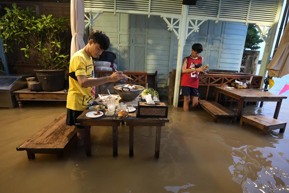 Customers of the riverside Chaopraya Antique Café enjoy themselves despite the extraordinary high water levels in the Chao Phraya River in Nonthaburi, near Bangkok, Thailand, Thursday, Oct. 7, 2021. The flood-hit restaurant has become an unlikely dining hotspot after fun-loving foodies began flocking to its water-logged deck to eat amid the lapping tide. Now, instead of empty chairs and vacant tables the “Chaopraya Antique Café” is as full as ever, offering an experience the canny owner has re-branded as “hot-pot surfing.” (AP Photo/Sakchai Lalit)