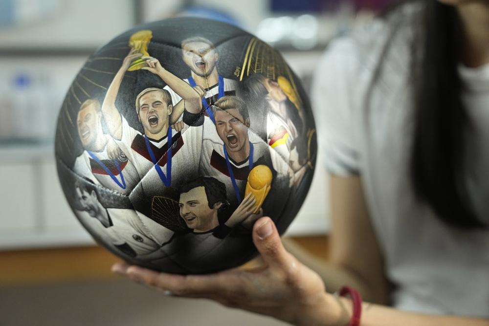 La artista plástica paraguaya Lili Cantero sostiene un balón de fútbol pintado a mano e ilustrado con integrantes de la selección de Alemania que disputó la Copa del Mundo de 2014, en San Lorenzo, Paraguay, el jueves 10 de noviembre de 2022. (Foto AP/Jorge Sáenz)