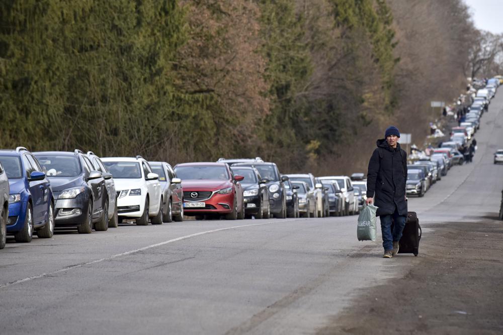 A man walks past a queue of cars heading to the Poland border near Shehyni, western Ukraine, Tuesday, March 1, 2022. Russian shelling pounded civilian targets in Ukraine's second-largest city again, and a 40-mile convoy of tanks and other vehicles threatened the capital. Ukraine's embattled president said the tactics were designed to force him into concessions in Europe's largest ground war in generations. (AP Photo/Pavlo Palamarchuk)