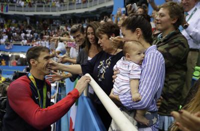 FILE - In this Tuesday, Aug. 9, 2016, file photo, United States' Michael Phelps celebrates winning his gold medal in the men's 200-meter butterfly with his mother Debbie, fiance Nicole Johnson and baby Boomer during the swimming competitions at the 2016 Summer Olympics in Rio de Janeiro, Brazil. Private, touching moment between loved ones won't be happening at the pandemic-delayed Tokyo Olympics. No spectators — local or foreign — will be allowed at the majority of venues, where athletes will hang medals around their own necks to protect against spreading the coronavirus. No handshakes or hugs on the podium, either. (AP Photo/Matt Slocum, File)
