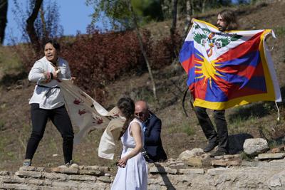 Un policía intenta detener a manifestantes que muestran una bandera tibetana y una pancarta con el mensaje "No a los juegos del genocidio" durante la ceremonia de encendido de la llama olímpica en la Antigua Olimpia, donde nacieron los antiguos Juegos Olímpicos, en el suroeste de Grecia, el lunes 18 de octubre de 2021. La llama será trasladada hasta Beijing, China, que acogerá los Juegos de Invierno entre el 4 y el 20 de febrero de 2022. (AP Foto/Thanassis Stavrakis)
