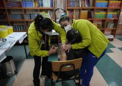 Los trabajadores de la salud le dan a un niño una vacuna de refuerzo de la vacuna pediátrica Pfizer COVID-19 en la Escuela Paul Harris en Santiago, Chile, el viernes 13 de mayo de 2022. (AP Foto/Esteban Félix)