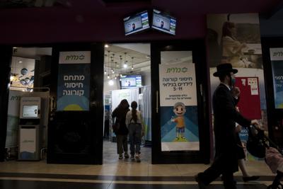 Una mujer acompaña a su hija a vacunarse contra el coronavirus en un centro de vacunación improvisado en el complejo Cinema City de Jerusalén, el 23 de noviembre de 2021. (AP Foto/Maya Alleruzzo)