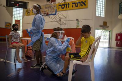 Personal médico hace pruebas de coronavirus a niños israelíes en una cancha de basquetbol convertida en centro de pruebas en Binyamina, Israel, el martes 29 de junio de 2021. (AP Foto/Ariel Schalit)