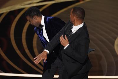 Will Smith, right, hits presenter Chris Rock on stage while presenting the award for best documentary feature at the Oscars on Sunday, March 27, 2022, at the Dolby Theatre in Los Angeles. (AP Photo/Chris Pizzello)