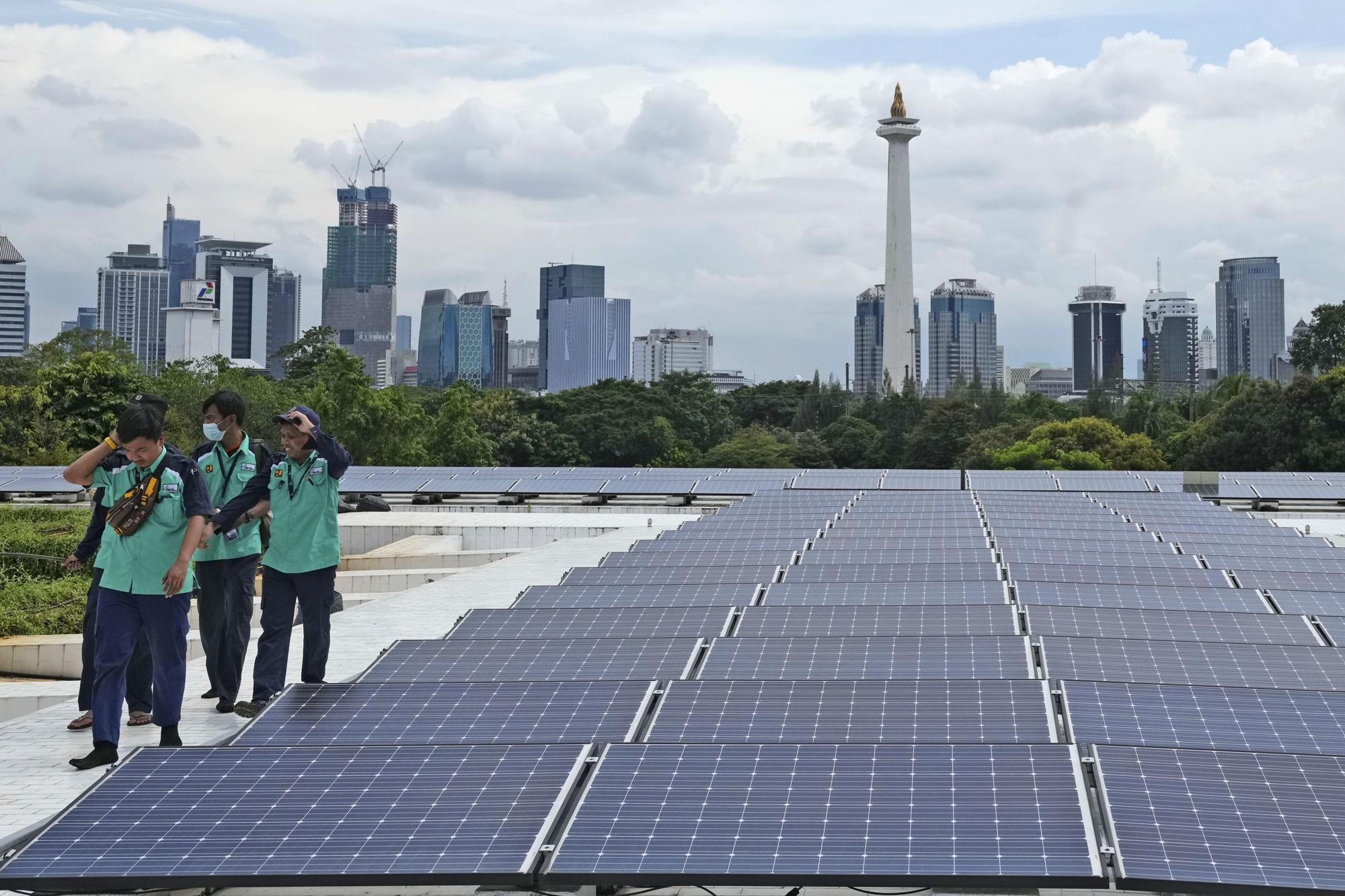 Los trabajadores caminan cerca de los paneles solares que proporcionan energía eléctrica parcial a la Mezquita Istiqlal mientras se ve el horizonte de la ciudad al fondo, en Yakarta, Indonesia, el miércoles 29 de marzo de 2023. Una importante renovación en 2019 instaló más de 500 paneles solares en la amplia mezquita. techo, ahora una importante y limpia fuente de electricidad de Istiqlal.  (Foto AP/Tatán Syuflana)