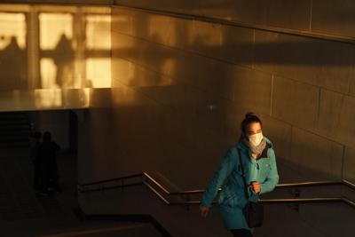 Fotografía de archivo del 2 de diciembre de 2020 de una mujer con mascarilla para renar los contagios de COVID-19 saliendo de un paso peatonal hacia la calle mientras el sol se pone en Moscú. (AP Foto/Alexander Zemlianichenko)