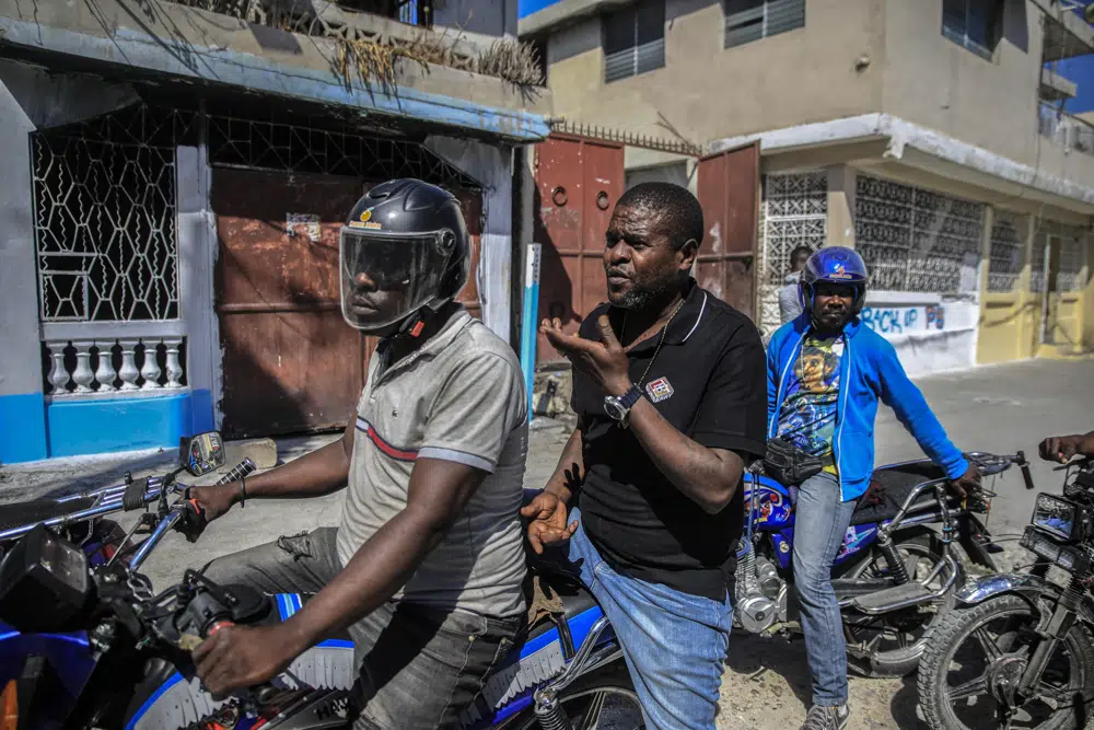 Jimmy Cherizier, líder de la pandilla "G9 et Famille", habla con miembros de su grupo sentado en la parte trasera de una motocicleta en su distrito de Delmas 6 en Puerto Príncipe, Haití, el martes 24 de enero de 2023. Cherizier, mejor conocido por su apodo de infancia Barbecue, se ha convertido en el nombre más reconocido en Haití. (AP Foto/Odelyn Joseph)
