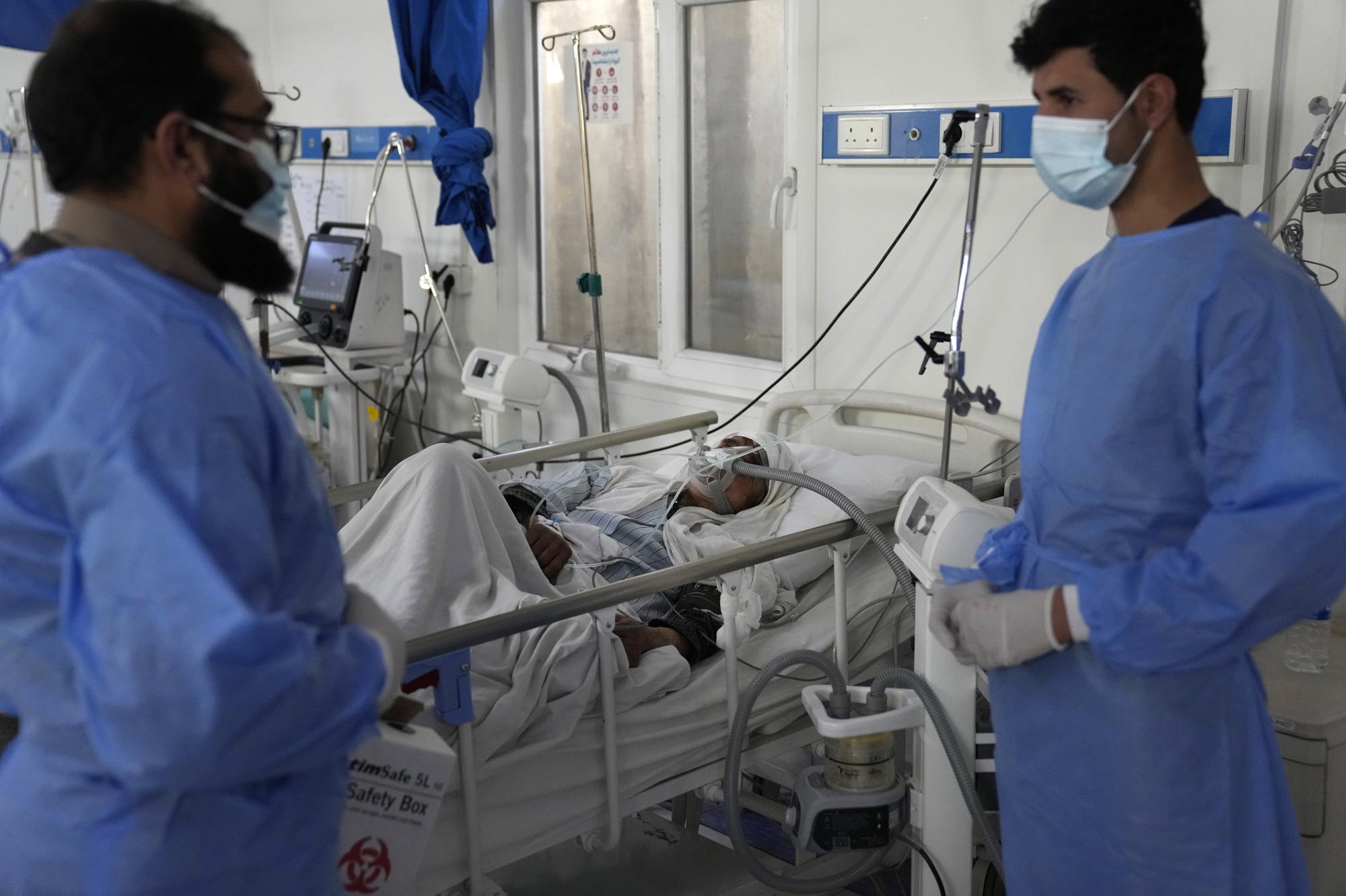 Two doctors talk as an Afghan patient with COVID-19 lies on a bed in the intensive care unit of the Afghan Japan Communicable Disease Hospital, in Kabul, Afghanistan, Monday, Feb. 7, 2022. All but five of 38 COVID treatment hospitals that once operated in Afghanistan have been forced to close for lack of doctors, medicines and even heat. This comes as an economically devastated Afghanistan last week experienced a 67% increase in the numbers of reported COVID cases, according to the World Health Organization. (AP Photo/Hussein Malla)