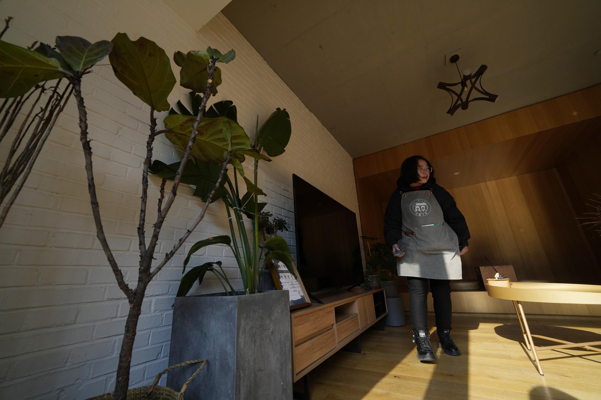 A local resident hired as a cleaner for a traditional courtyard house turned into lodging for tourists, inspects one of the room in Houheilong Miao, a village in Yanqing on the outskirts of Beijing, China, Wednesday, Jan. 5, 2022. The village has a view of the Olympics skiing venue in the distance. Its 20 mostly vacant traditional courtyard houses have been turned into lodgings and a cafe dubbed the "Winter Olympic Home." (AP Photo/Ng Han Guan)