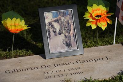 Un retrato de Gilberto De Jesús Campo es colocada en su tumba en el cementerio Jardín de Paz por su hermana Carmen Campo en el marco de otro aniversario de la invasión militar estadounidense, en la Ciudad de Panamá, el lunes 20 de diciembre de 2021. El 20 de diciembre de 1989 la acción militar expulsó del poder al dictador Manuel Noriega y causó la muerte de cientos de panameños, entre civiles y militares, según reportes oficiales. (Foto AP/Arnulfo Franco)