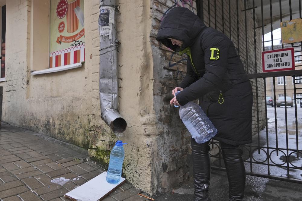 Kateryna Luchkina, a 31-year-old worker at Kyiv’s Department of Health, collects rainwater from a drainpipe in Kyiv, Ukraine, on Thursday. Nov. 24, 2022. Residents of Ukraine's bombed but not cowed capital roamed the streets with empty bottles in search of water and crowded into cafés for warmth, light and power Thursday, switching defiantly into survival mode after new Russian missile strikes the previous day plunged the city of 3 million and much of the country into the dark in winter.  (AP Photo/John Leicester)