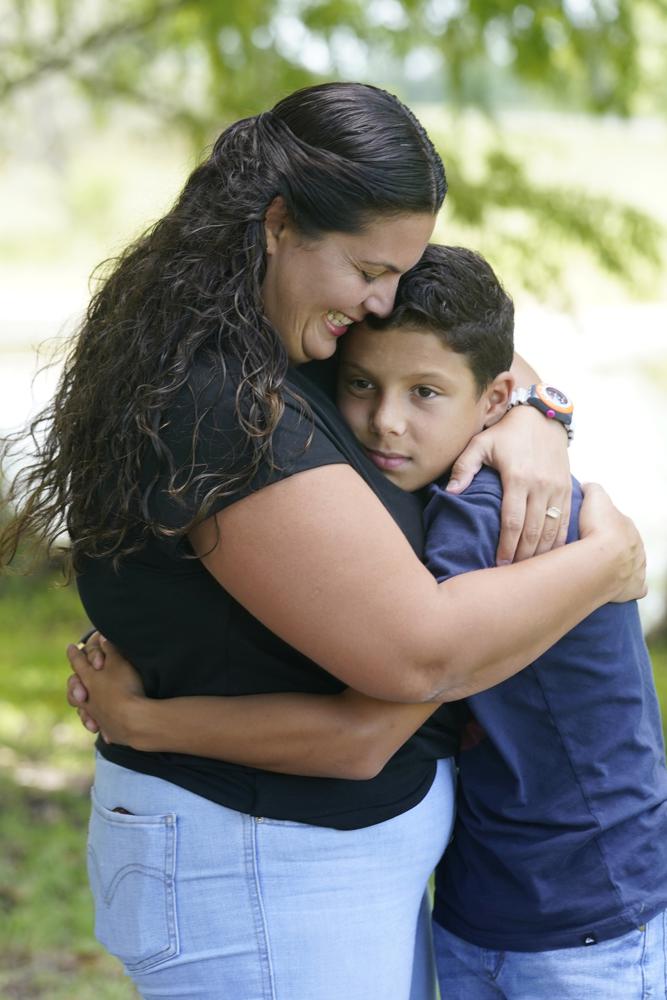 Ana Merino abraza a su hijo, José Antonio Macedo, de 11 años, el jueves 14 de julio de 2022 en Sunrise, Florida. La familia huyó de Venezuela y en diciembre cruzó la frontera de Estados Unidos con México. Son parte de un numeroso grupo de venezolanos que quedaron afuera de un programa de protección temporal para algunos extranjeros que no han regularizado su situación migratoria, conocido como TPS. El gobierno acaba de extenderlo para los que llegaron antes del 9 de hasta marzo de 2021. (AP Foto/Marta Lavandier)