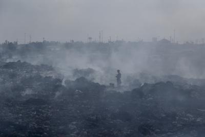 Un hombre cruza una una montaña de basura en medio del humo de fogatas en Dandora, el basural más grande de Nairobi, Kenia, el 7 de septiembre de 2021. (AP Foto/Brian Inganga, File)