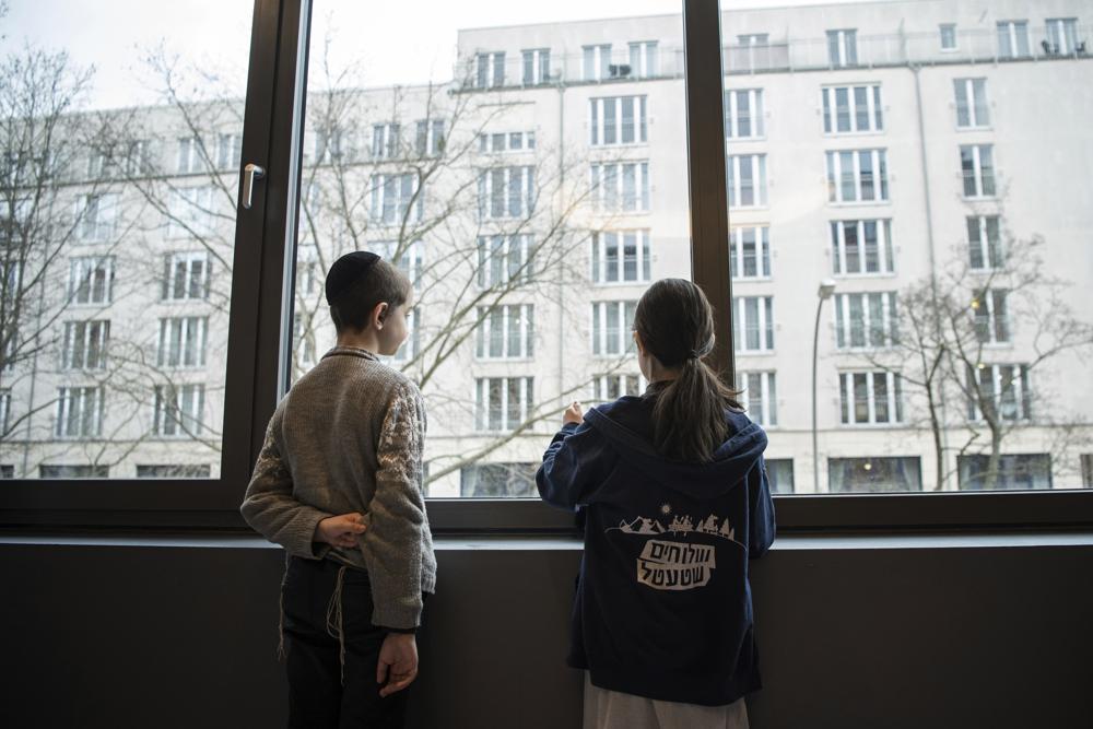 Chłopiec i dziewczynka z sierocińca w Odessie na Ukrainie wyglądają przez okno po przybyciu do hotelu w Berlinie, piątek, 4 marca 2022 r. Ponad 100 żydowskich dzieci uchodźców, które zostały ewakuowane z domu opieki zastępczej na rozdartej wojną Ukrainie i przejechały autobusem przez Europę, przybyło do Berlina. (AP Photo/Steffi Loos)