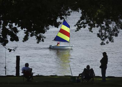 ARCHIVO - Un velero de la St. Joseph Junior Foundation Summer Sailling School pasa junto a personas pescando en el río St. Joseph en Michigan el 15 de junio del 2022. El cambiante coronavirus ha arrancado el verano en Estados Unidos con muchas infecciones, pero relativamente pocas muertes en comparación con encarnaciones previas. El COVID-19 sigue matando a centenares de estadounidenses cada día, pero no es tan peligroso como lo fue el otoño y el invierno pasados. (Don Campbell/The Herald-Palladium vía AP)