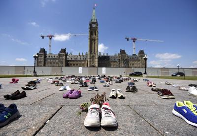 En esta fotografía del viernes 4 de junio de 2021 se ven flores secas que fueron colocadas dentro de un par de zapatos deportivos de niño en una ofrenda improvisada instalada en la Colina del Parlamento, en Ottawa, para los 215 menores cuyos restos fueron encontrados en terrenos del antiguo internado de Kamloops, en Columbia Británica. (Justin Tang/The Canadian Press vía AP)