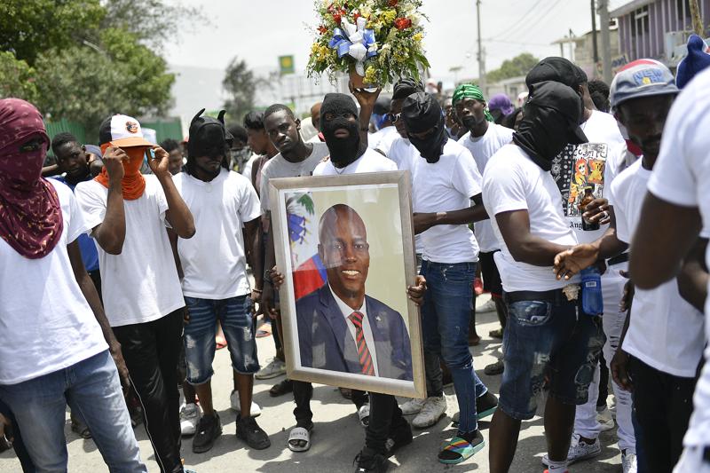Members of the gang led by Jimmy Cherizier, alias Barbecue, a former police officer who heads a gang coalition known as G9 Family and Allies, carry a photo of slain President Jovenel Moise during a march to demand justice for his murder, in La Saline neighborhood of Port-au-Prince, Haiti, Monday, July 26, 2021. Moise was assassinated on July 7 at his home. (AP Photo/Matias Delacroix)