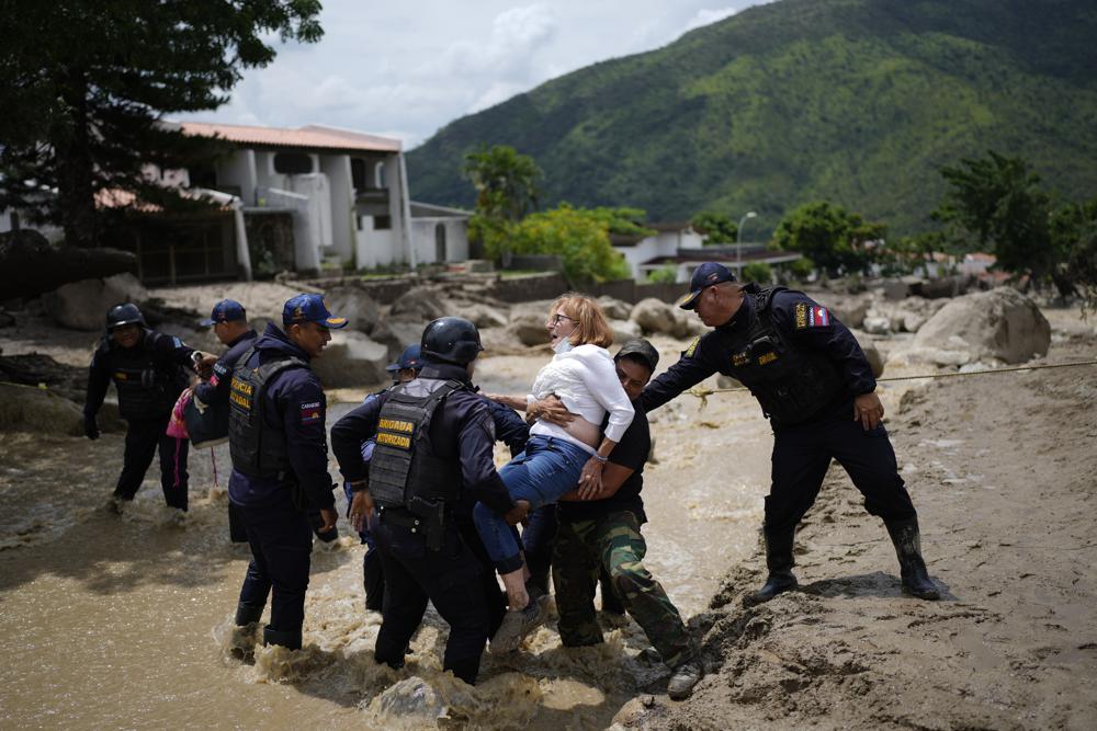 Policías cargan a una mujer por una calle inundada en El Castaño, Venezuela, el martes 18 de octubre de 2022. (AP Foto/Ariana Cubillos)