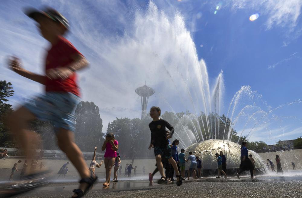 The International Fountain at Seattle Center is packed with children as they run from the water that is showering on them Wednesday, July 27, 2022 in Seattle. (Ellen M. Banner/The Seattle Times via AP)
