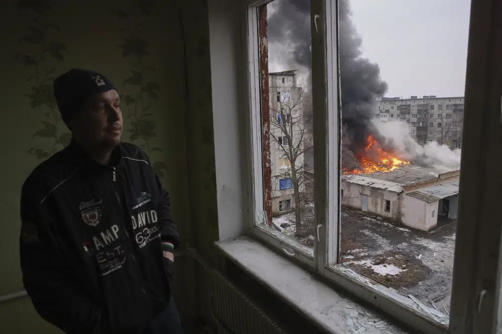 A local resident stands at the window as smoke raises from the burning building after the Russian shelling in the town of Chasiv Yar, the site of the heaviest battles with the Russian troops, Donetsk region, Ukraine, Monday, Feb. 27, 2023. (AP Photo/Yevhen Titov)