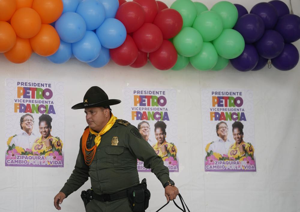 A police officer walks past posters of Historical Pact coalition presidential candidate Gustavo Petro and his running mate Francia Marquez during a closing campaign rally in Zipaquira, Colombia, Sunday, May 22, 2022. Elections are set for May 29. (AP Photo/Fernando Vergara)