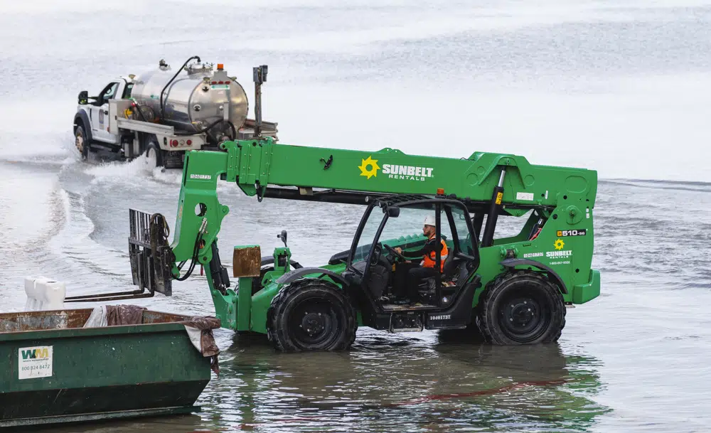 A worker lift a barricades with a forklift as truck drives through the flooded tarmac at the Fort Lauderdale-Hollywood International Airport on Thursday, April 13, 2023. (David Santiago/Miami Herald via AP)