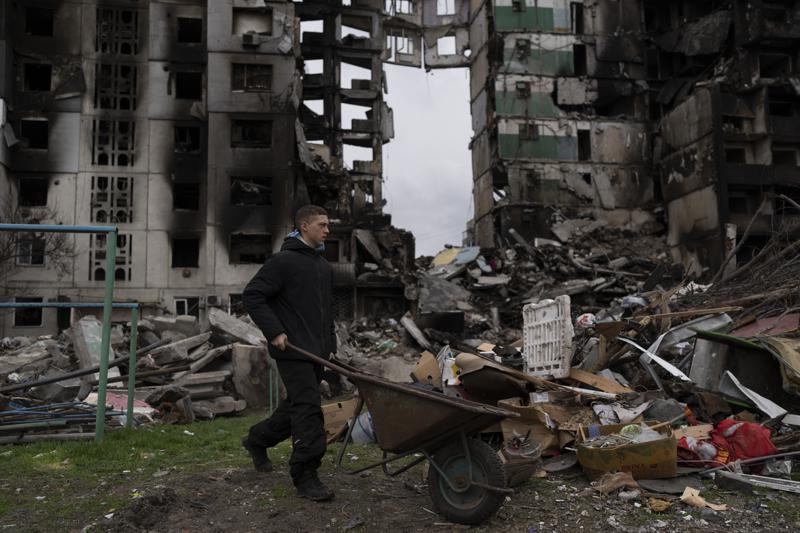 Un joven empuja una carretilla frente a un edificio residencial destruido, el domingo 10 de abril de 2022, en la localidad de Borodyanka, Ucrania. (AP Foto/Petros Giannakouris)