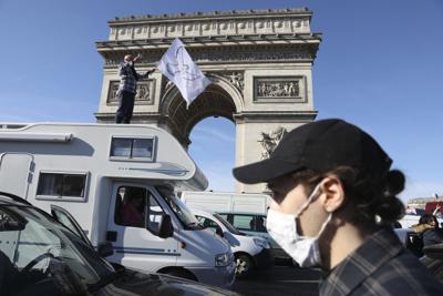 ARCHIVO - Un manifestante se para encima de una autocaravana mientras un convoy pasa por el Arco del Triunfo en la avenida de los Campos Elíseos, el sábado 12 de febrero de 2022 en París, en protestas contra las restricciones del virus inspiradas en el "Convoy de la Libertad" de Canadá. El viernes 18 de febrero de 2022, The Associated Press informó sobre historias que circulaban en línea afirmando incorrectamente que la policía parisina multó a los manifestantes por llevar la bandera francesa y decir la palabra "libertad". Pero se entregaron boletos a los manifestantes por delitos relacionados con "participar en una protesta prohibida". (AP Photo/Adrienne Surprenant, Archivo)