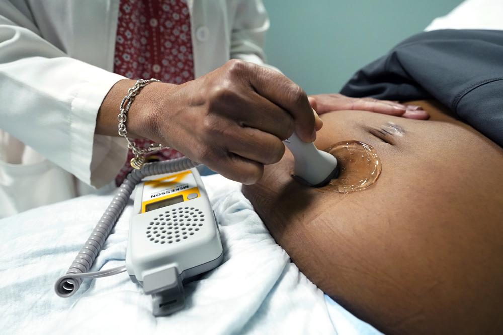 A doctor uses a hand-held Doppler probe on a pregnant woman